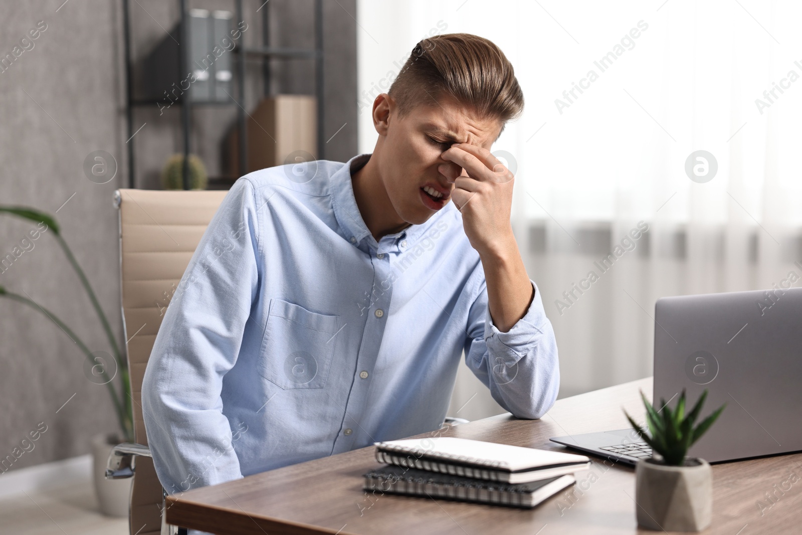 Photo of Young man suffering from sinusitis at wooden table indoors