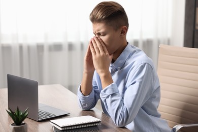 Photo of Young man suffering from sinusitis at wooden table indoors