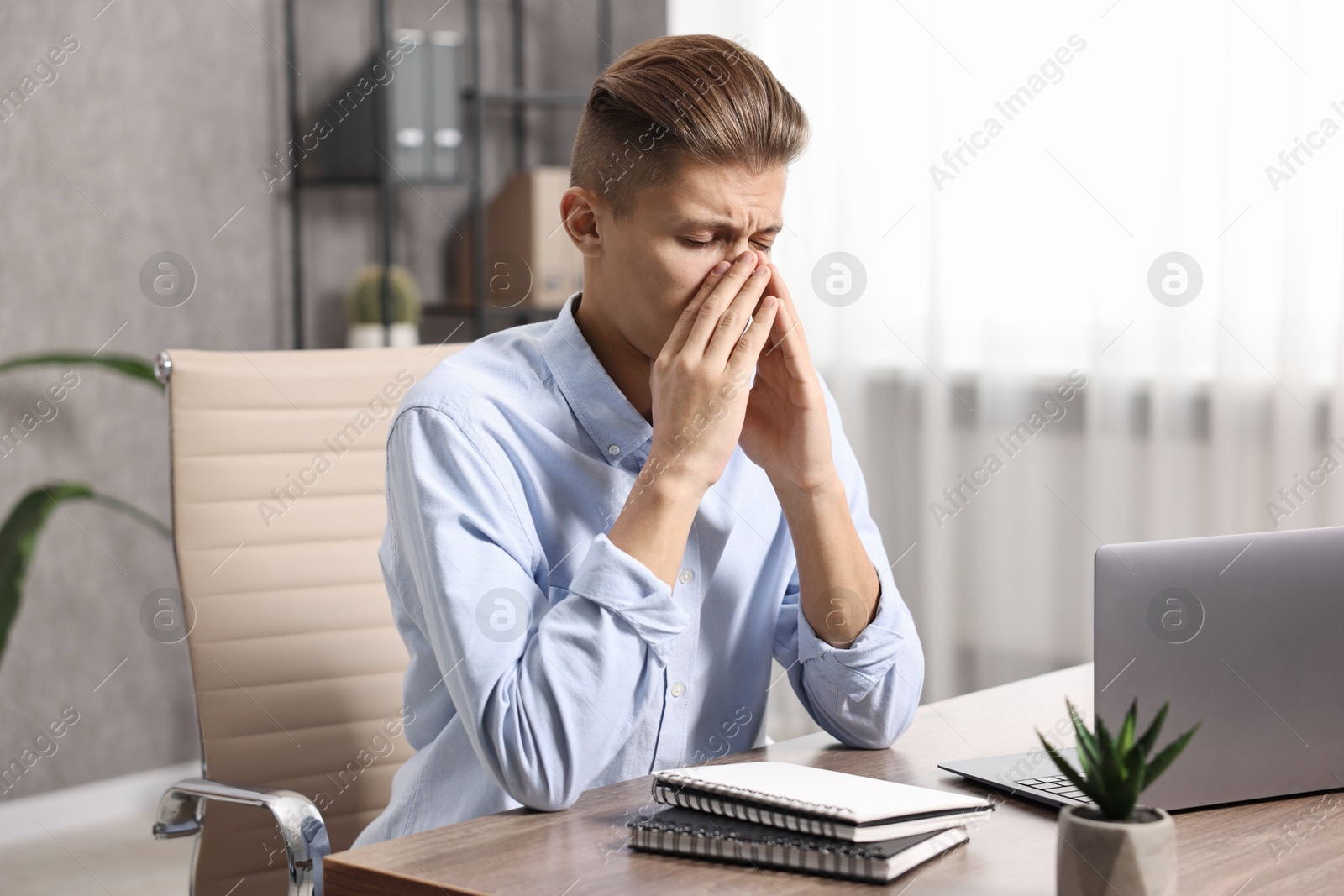 Photo of Young man suffering from sinusitis at wooden table indoors