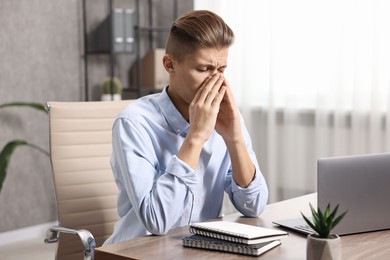 Photo of Young man suffering from sinusitis at wooden table indoors