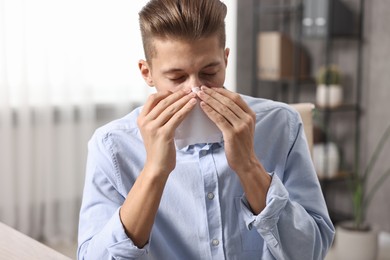 Young man with tissue suffering from sinusitis indoors