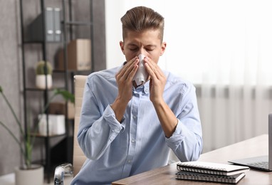 Young man with tissue suffering from sinusitis at wooden table indoors