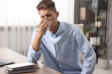 Young man with tissue suffering from sinusitis at wooden table indoors