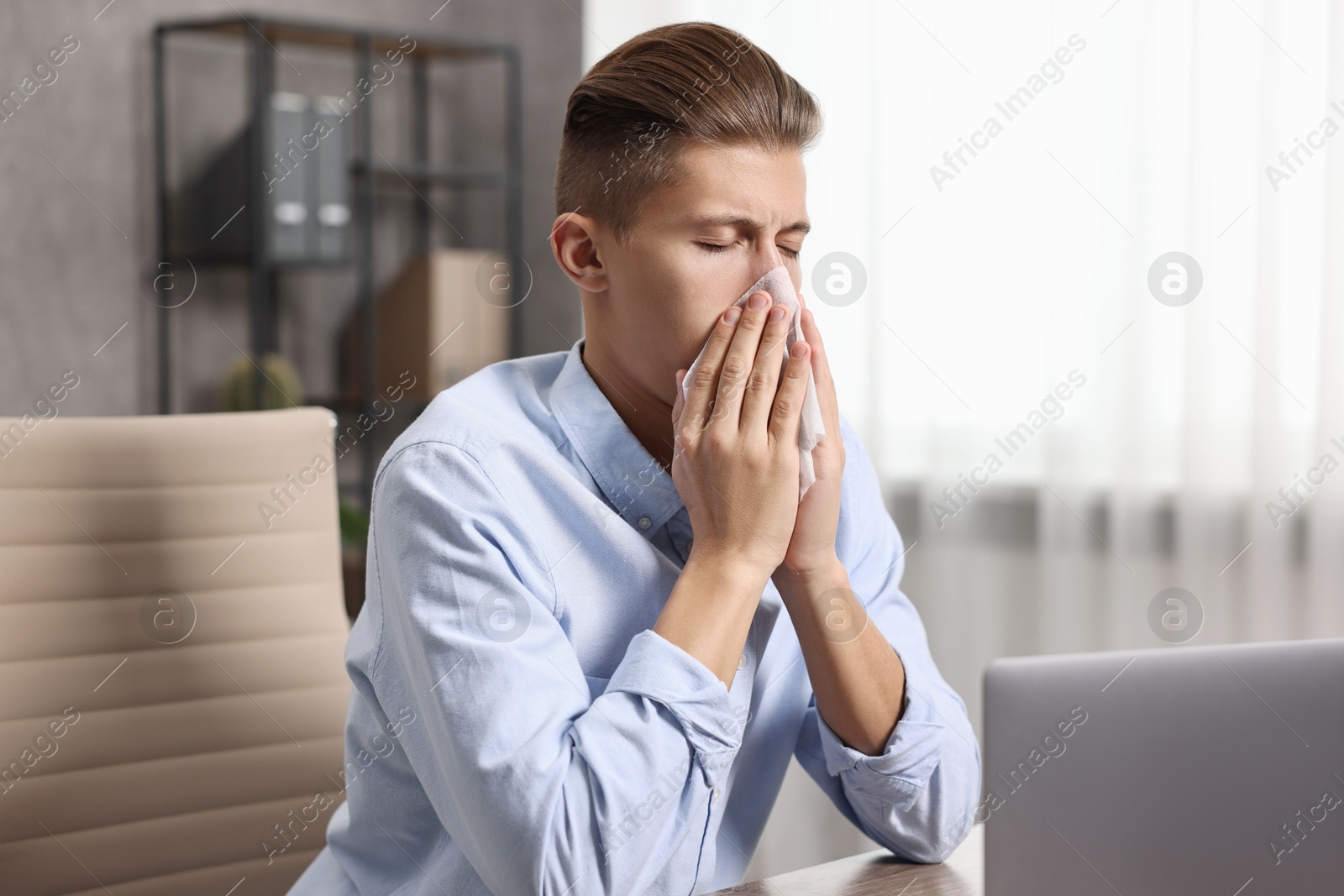 Photo of Young man with tissue suffering from sinusitis at wooden table indoors