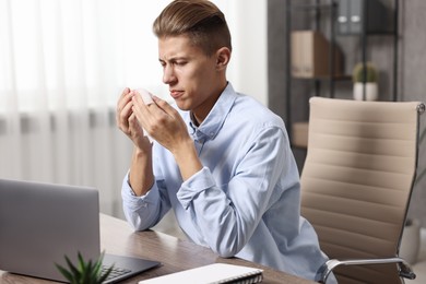 Photo of Young man with tissue suffering from sinusitis at wooden table indoors