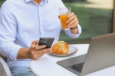 Man having breakfast and using smartphone in outdoor cafe, closeup