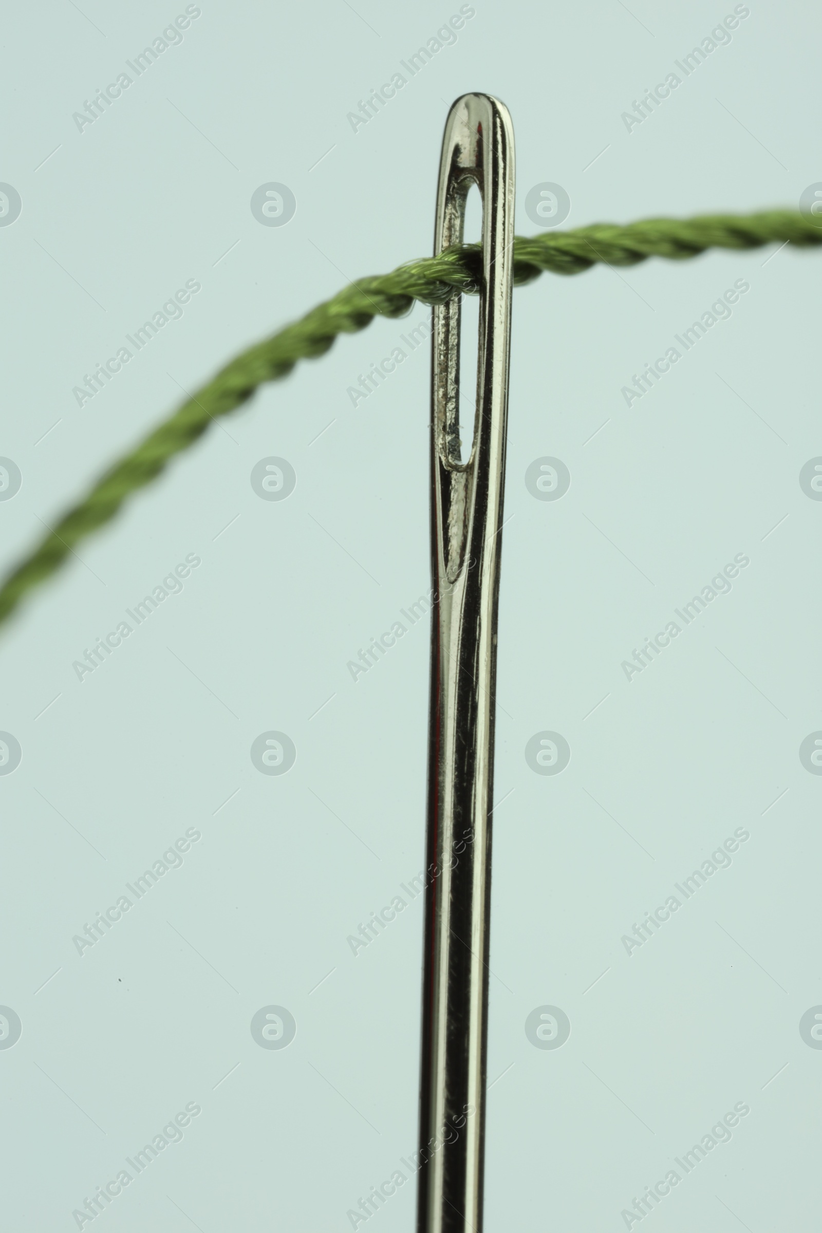 Photo of Sewing needle with green thread on white background, closeup