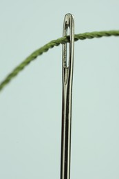 Photo of Sewing needle with green thread on white background, closeup