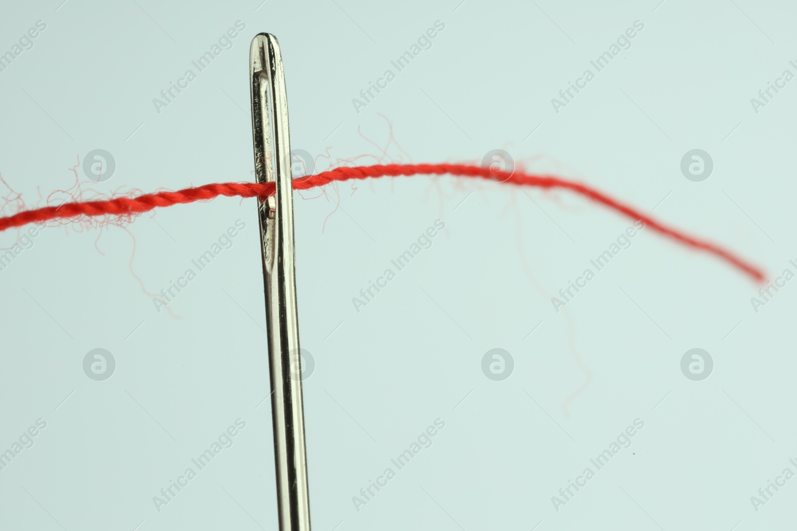 Photo of Sewing needle with red thread on white background, closeup