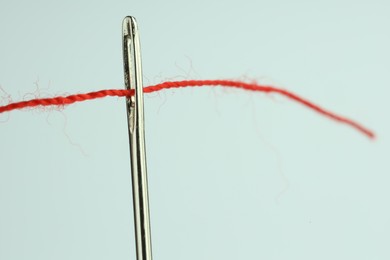 Photo of Sewing needle with red thread on white background, closeup