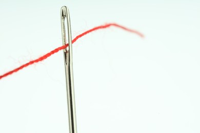 Photo of Sewing needle with red thread on white background, closeup