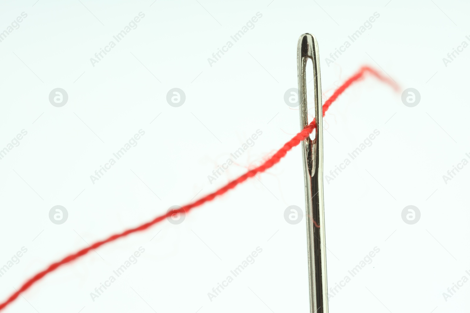 Photo of Sewing needle with red thread on white background, closeup