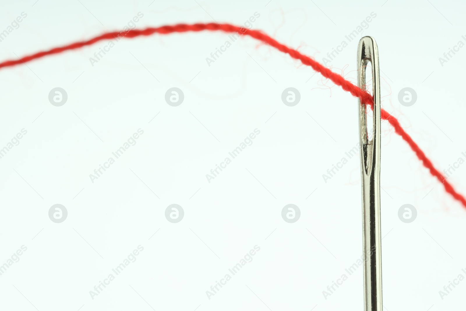 Photo of Sewing needle with red thread on white background, closeup