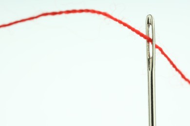 Photo of Sewing needle with red thread on white background, closeup