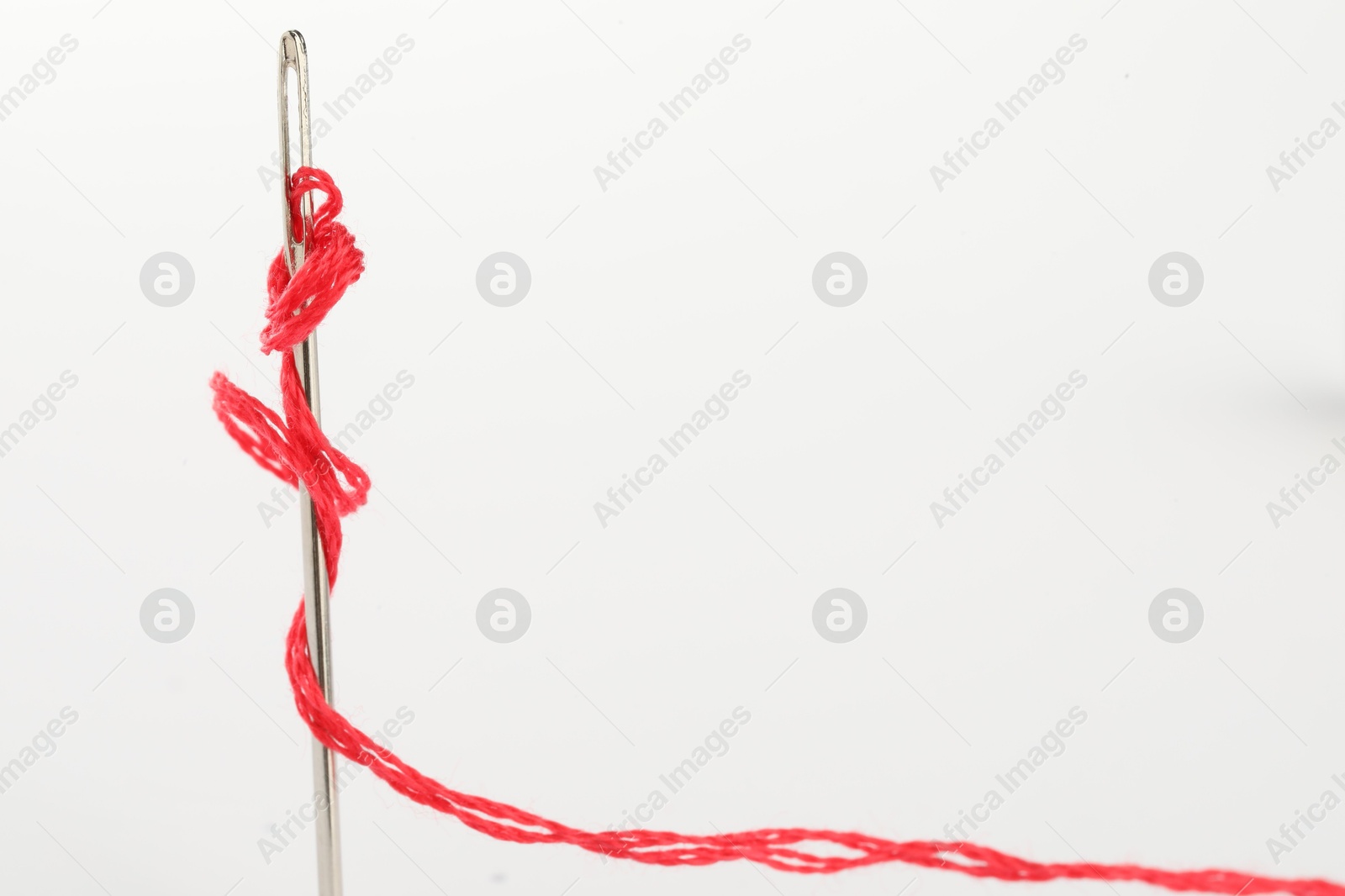 Photo of Sewing needle with red thread isolated on white, closeup