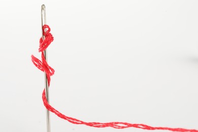 Photo of Sewing needle with red thread isolated on white, closeup