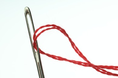 Sewing needle with red thread on white background, closeup