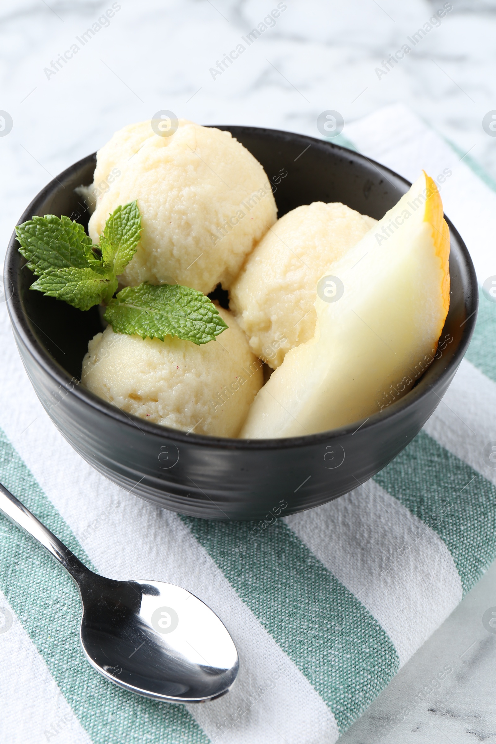 Photo of Scoops of tasty melon sorbet with mint in bowl and spoon on white table, closeup