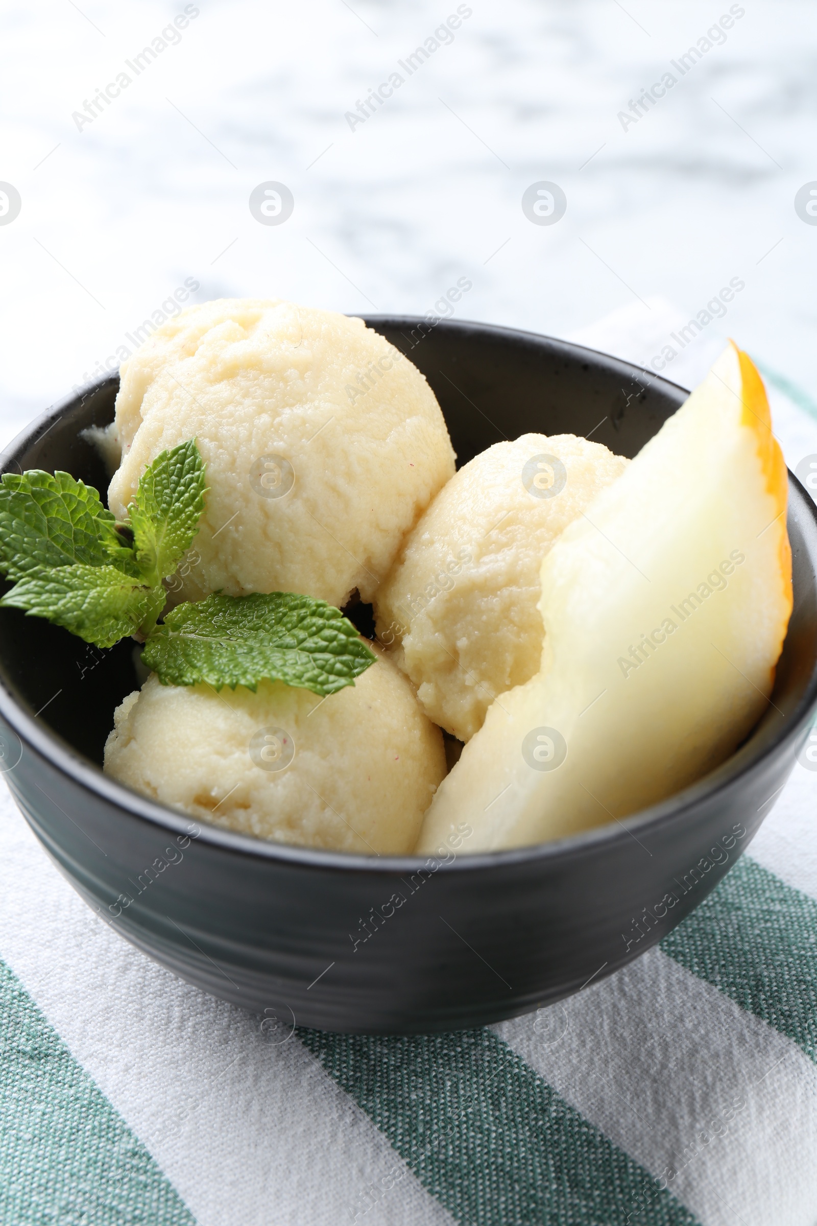 Photo of Scoops of tasty melon sorbet with mint and fresh fruit in bowl on white table, closeup