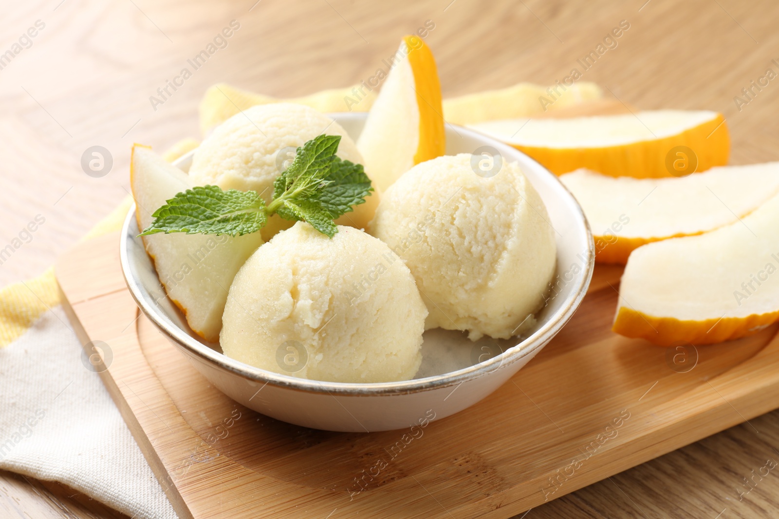 Photo of Scoops of tasty melon sorbet with fresh fruit and mint in bowl on wooden table, closeup