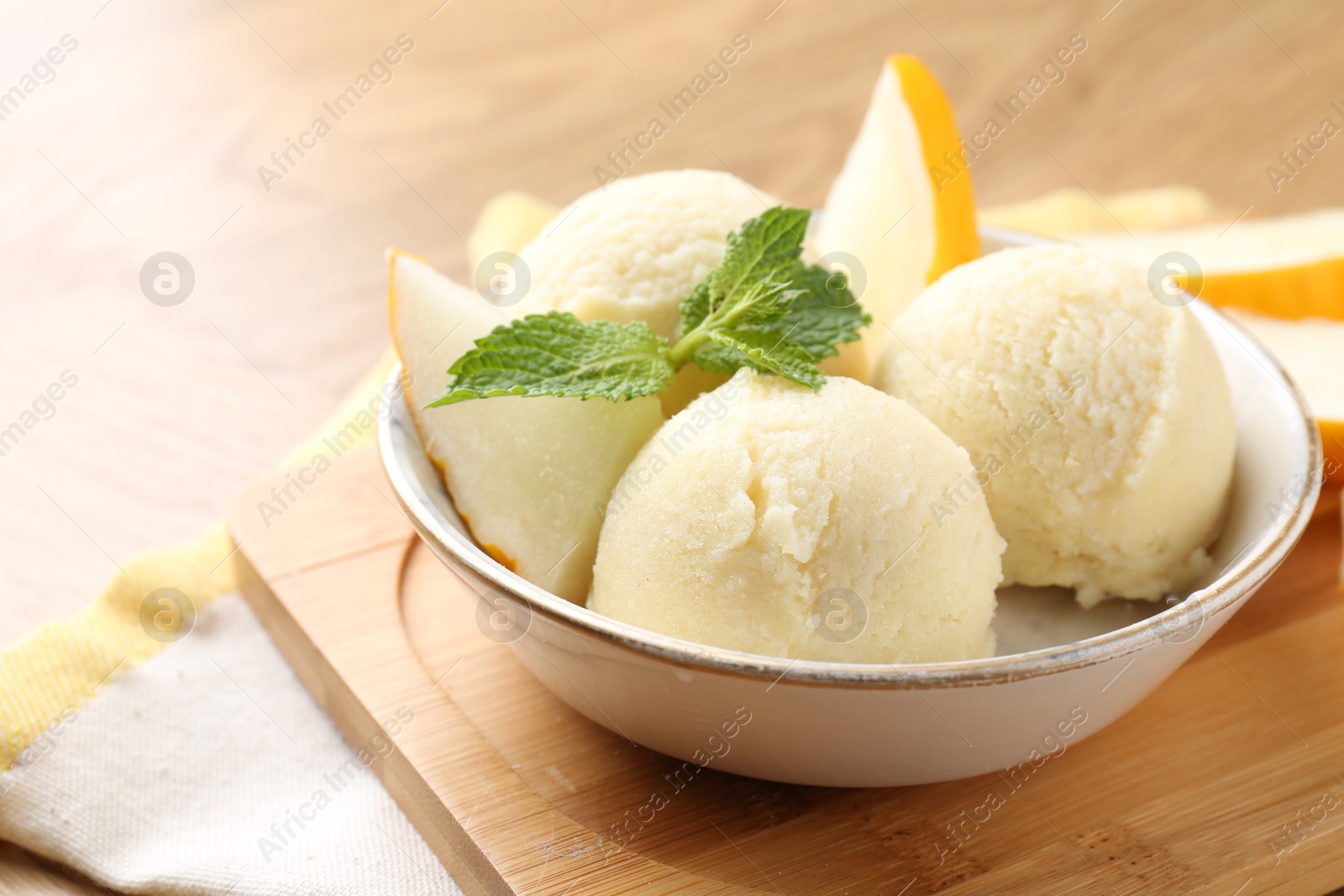 Photo of Scoops of tasty melon sorbet with fresh fruit and mint in bowl on wooden table, closeup