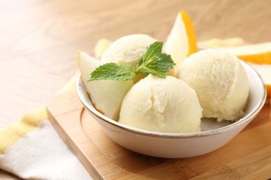 Scoops of tasty melon sorbet with fresh fruit and mint in bowl on wooden table, closeup