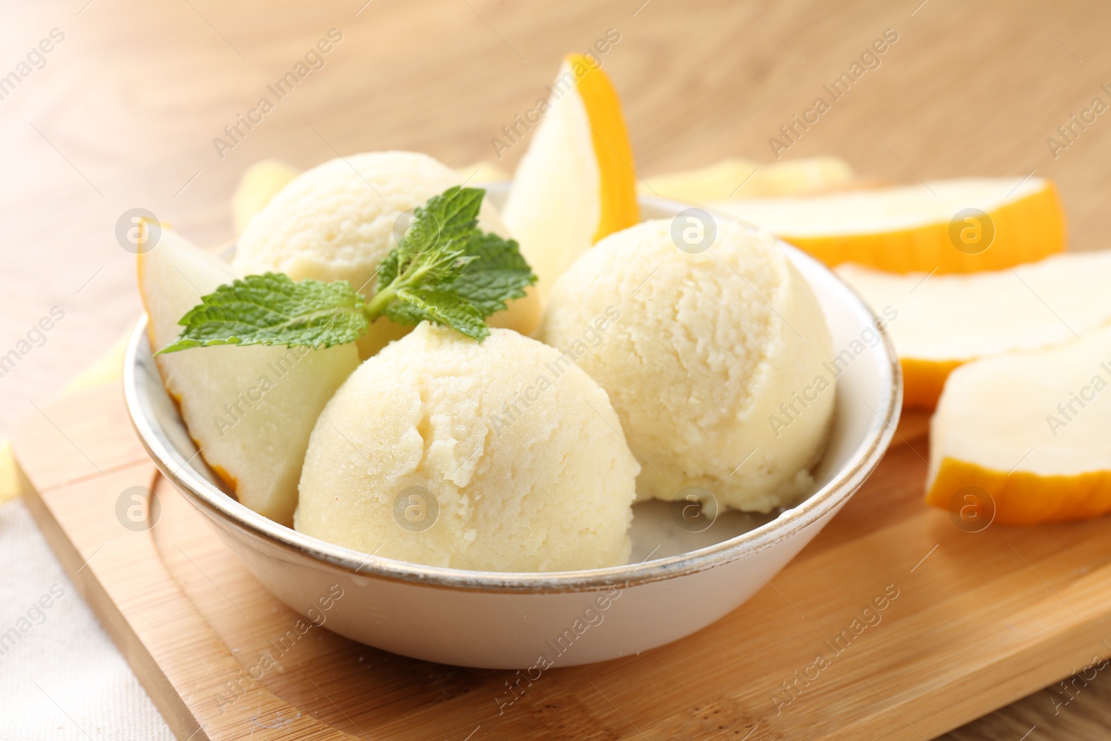 Photo of Scoops of tasty melon sorbet with fresh fruit and mint in bowl on wooden table, closeup