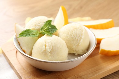 Scoops of tasty melon sorbet with fresh fruit and mint in bowl on wooden table, closeup