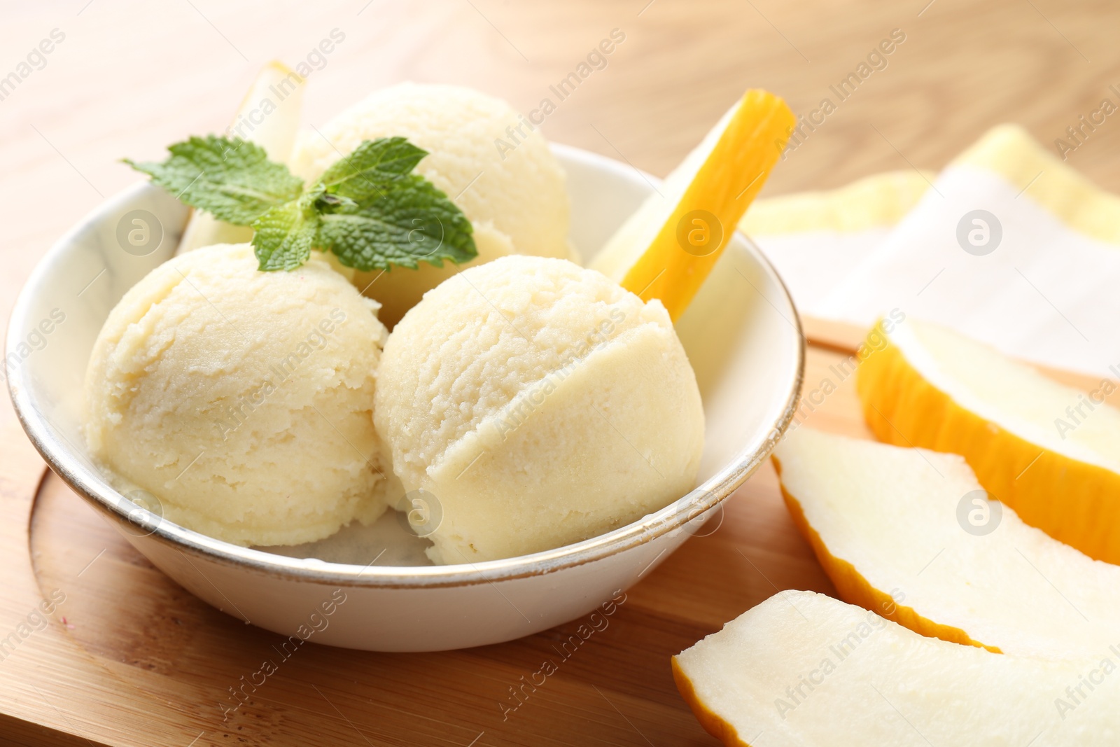 Photo of Scoops of tasty melon sorbet with mint in bowl and fresh fruit on table, closeup