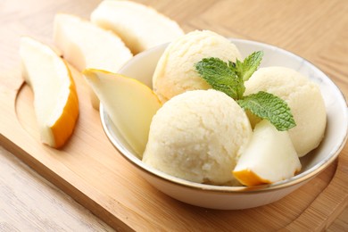 Photo of Scoops of tasty melon sorbet with mint in bowl and fresh fruit on wooden table, closeup