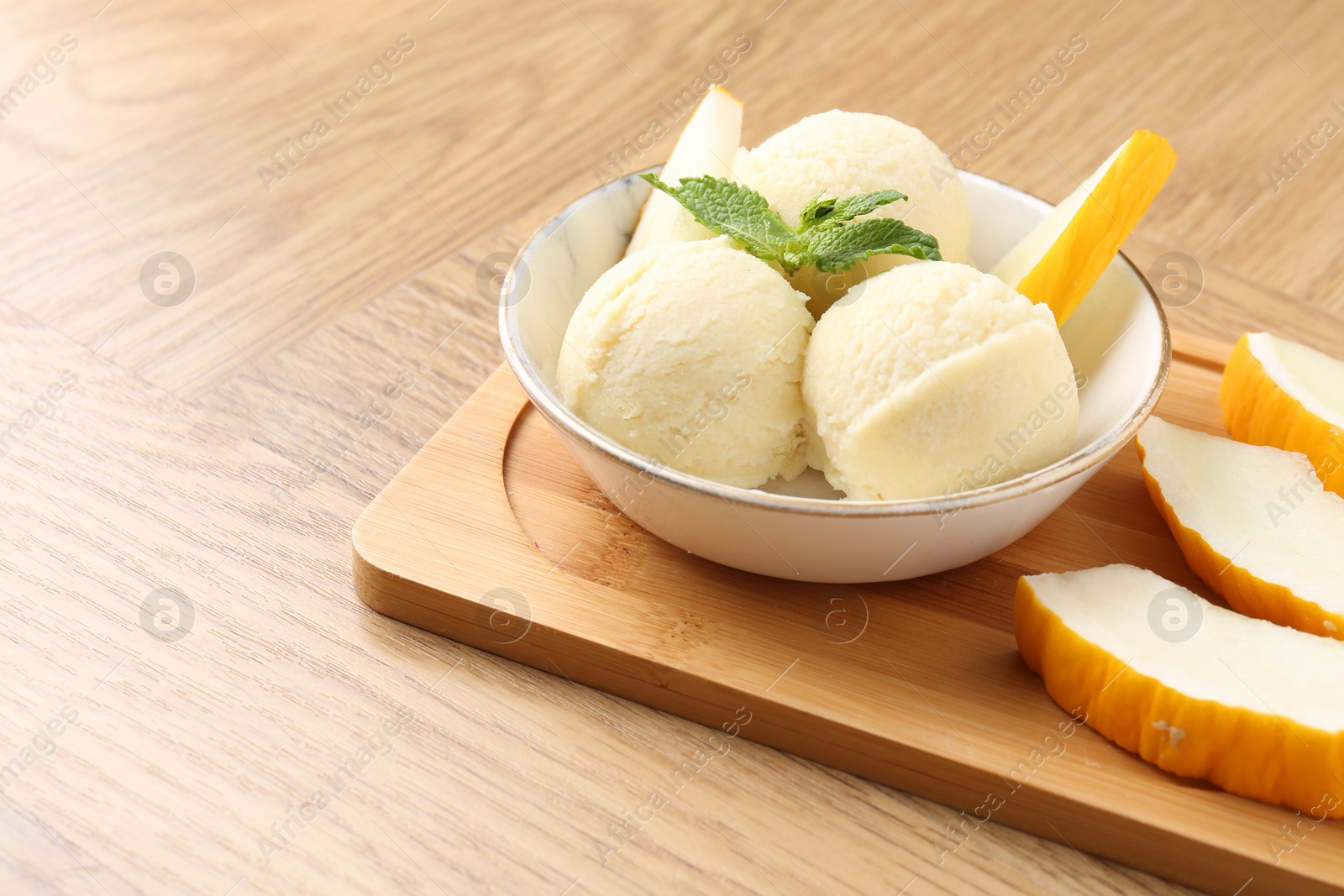 Photo of Scoops of tasty melon sorbet with mint in bowl and fresh fruit on wooden table, space for text