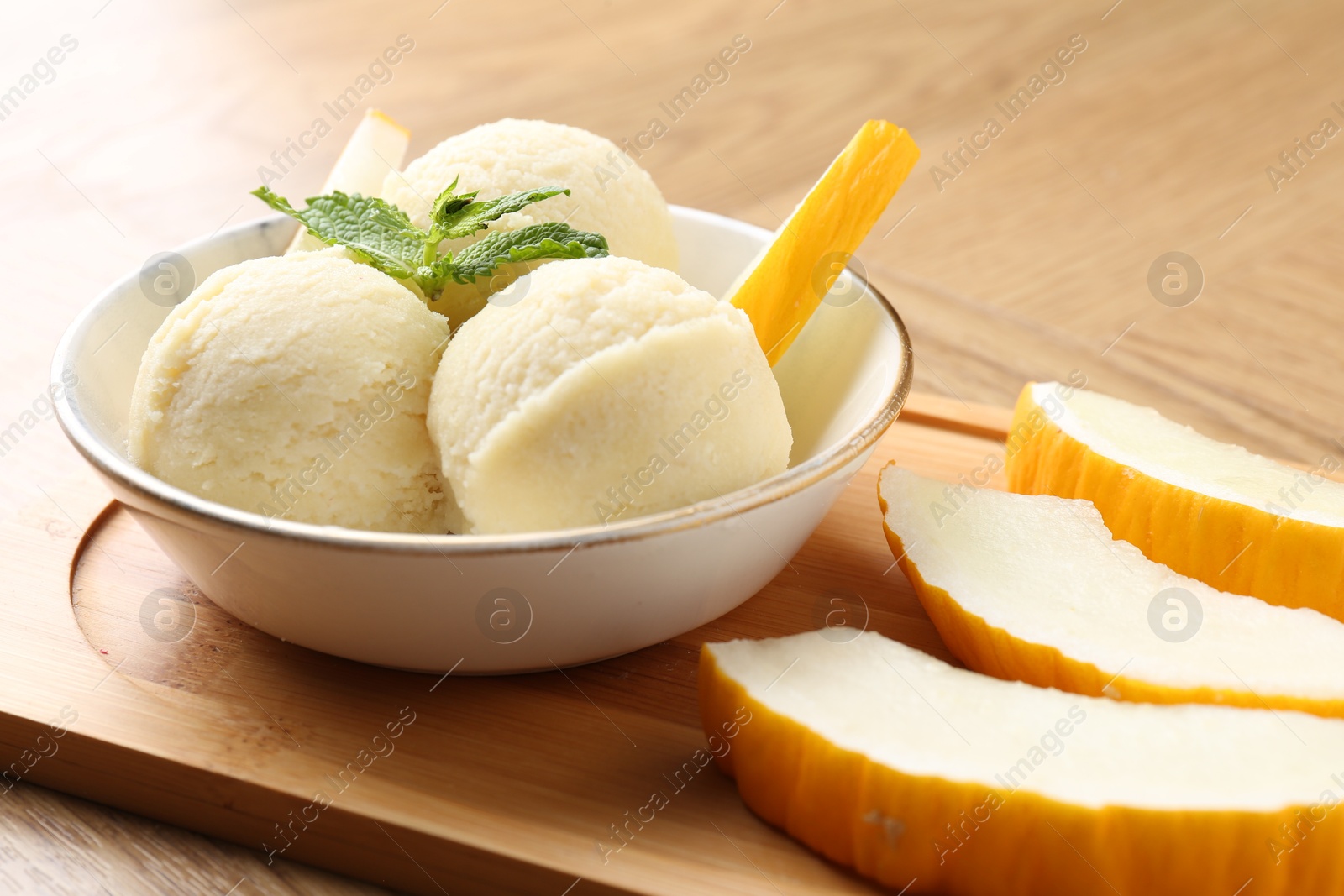 Photo of Scoops of tasty melon sorbet with mint in bowl and fresh fruit on wooden table, closeup