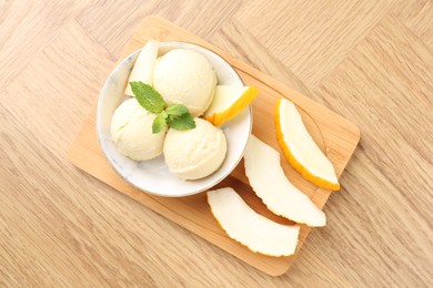 Photo of Scoops of tasty melon sorbet with mint in bowl and fresh fruit on wooden table, top view