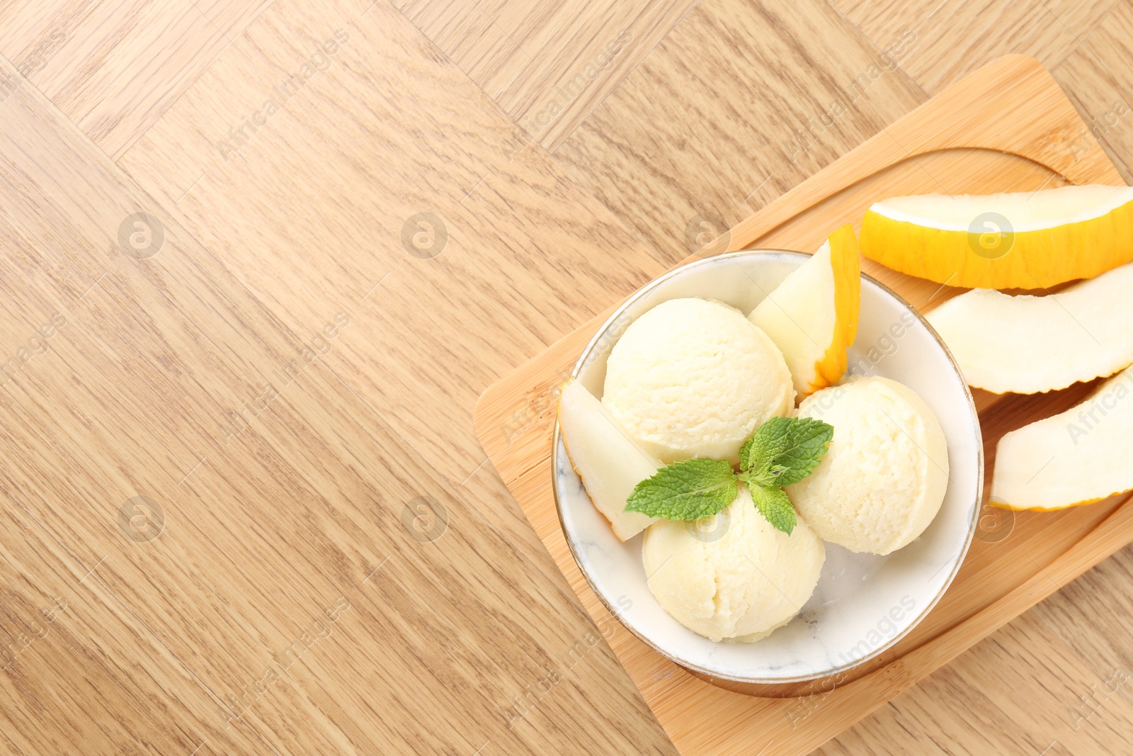 Photo of Scoops of tasty melon sorbet with mint in bowl and fresh fruit on wooden table, top view. Space for text