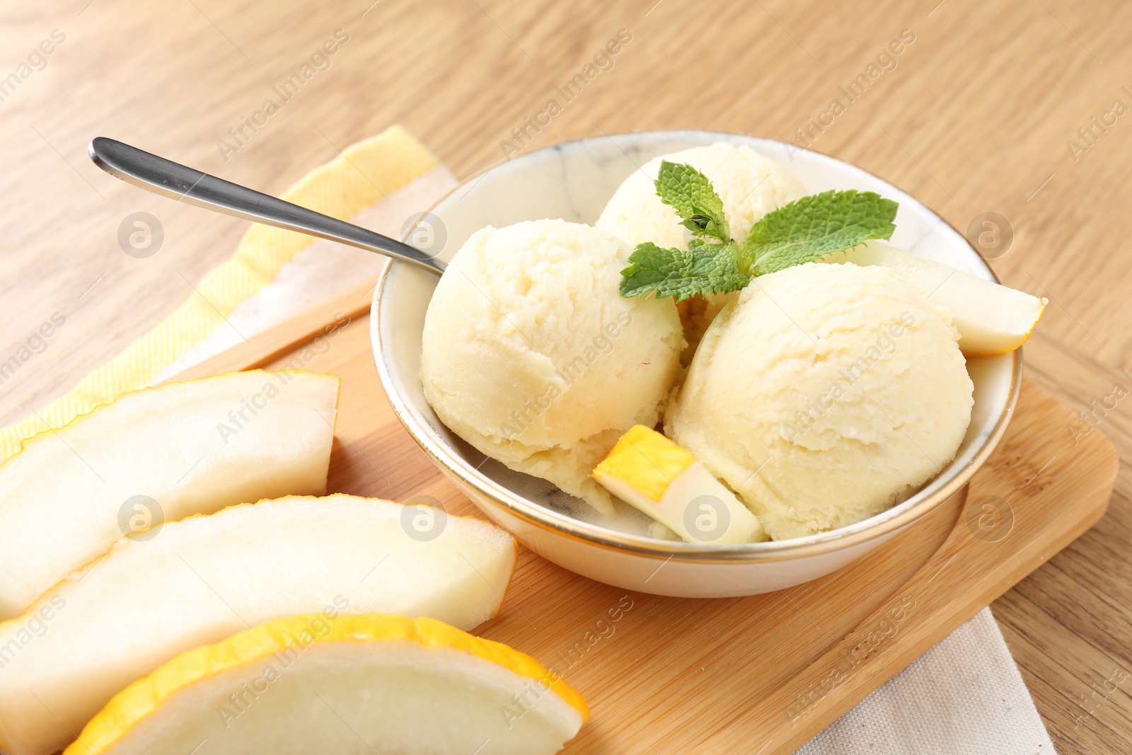 Photo of Scoops of tasty melon sorbet with mint in bowl and fresh fruit on wooden table, closeup