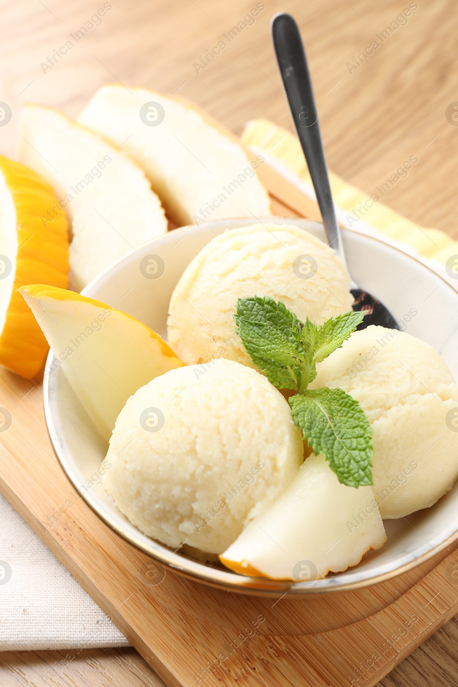 Photo of Scoops of tasty melon sorbet with mint in bowl and fresh fruit on wooden table, closeup