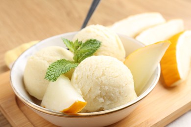 Photo of Scoops of tasty melon sorbet with fresh fruit and mint in bowl on table, closeup