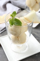 Photo of Scoops of melon sorbet with mint and fresh fruit in glass dessert bowl on grey table, closeup