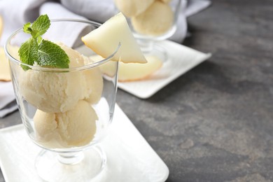 Photo of Scoops of melon sorbet with mint and fresh fruit in glass dessert bowl on grey table, closeup. Space for text