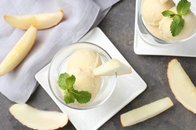 Scoops of melon sorbet with mint in glass dessert bowls and fresh fruit on grey table, flat lay