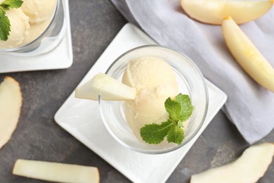 Scoops of melon sorbet with mint in glass dessert bowls and fresh fruit on grey table, flat lay