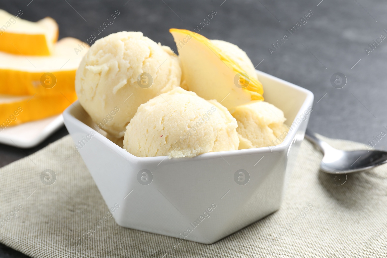 Photo of Scoops of tasty melon sorbet with fresh fruit in bowl on grey table, closeup