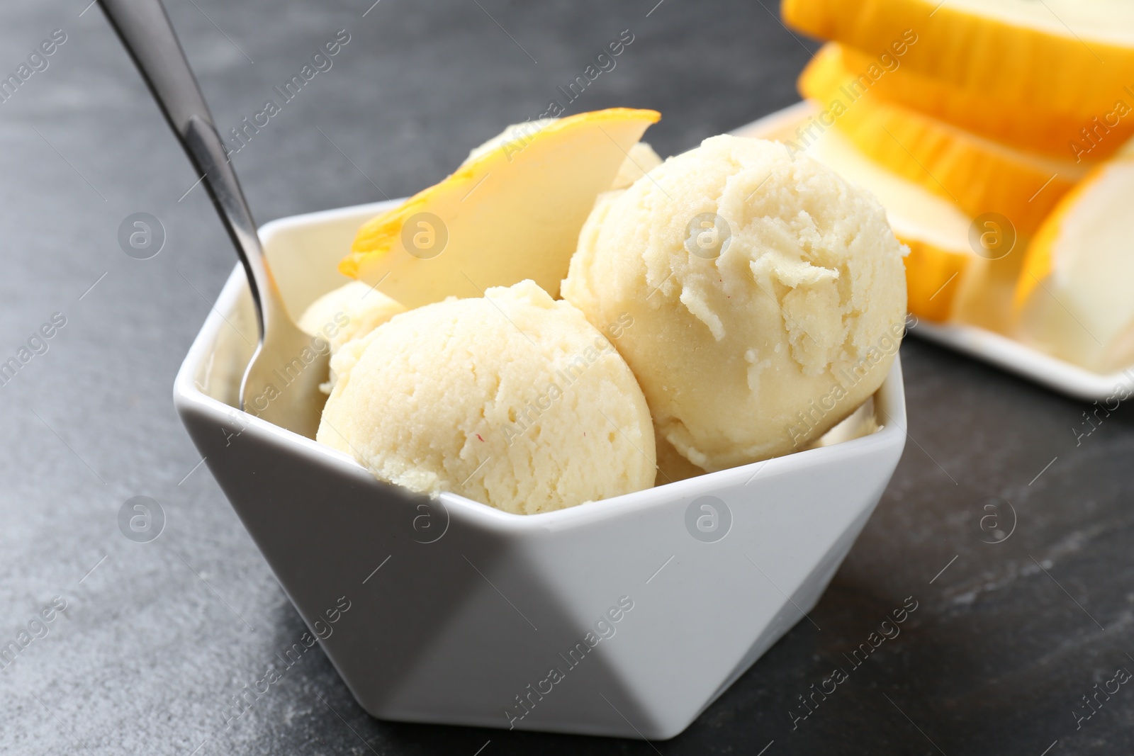 Photo of Scoops of tasty melon sorbet with fresh fruit and spoon in bowl on grey textured table, closeup