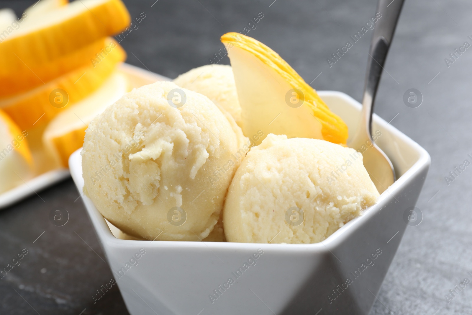 Photo of Scoops of tasty melon sorbet with fresh fruit and spoon in bowl on grey table, closeup