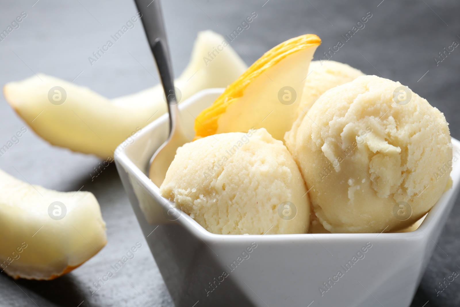 Photo of Scoops of tasty melon sorbet with fresh fruit and spoon in bowl on grey table, closeup