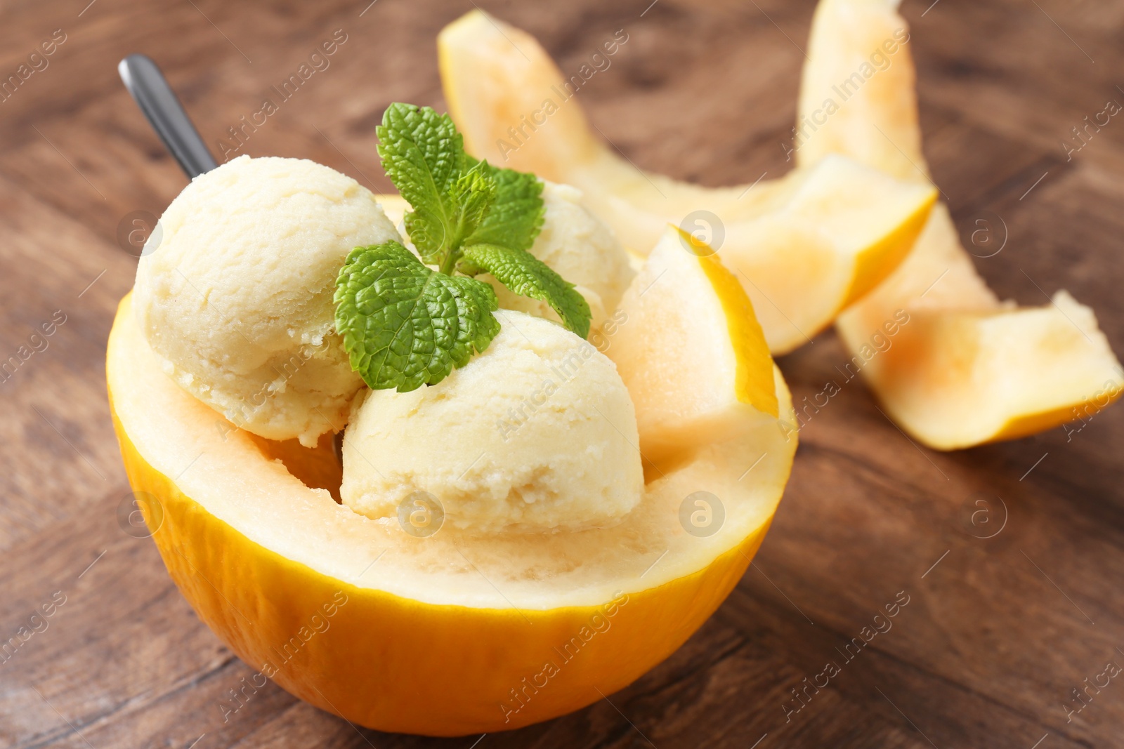 Photo of Scoops of tasty melon sorbet with mint in fresh fruit on wooden table, closeup