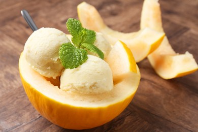 Photo of Scoops of tasty melon sorbet with mint in fresh fruit on wooden table, closeup