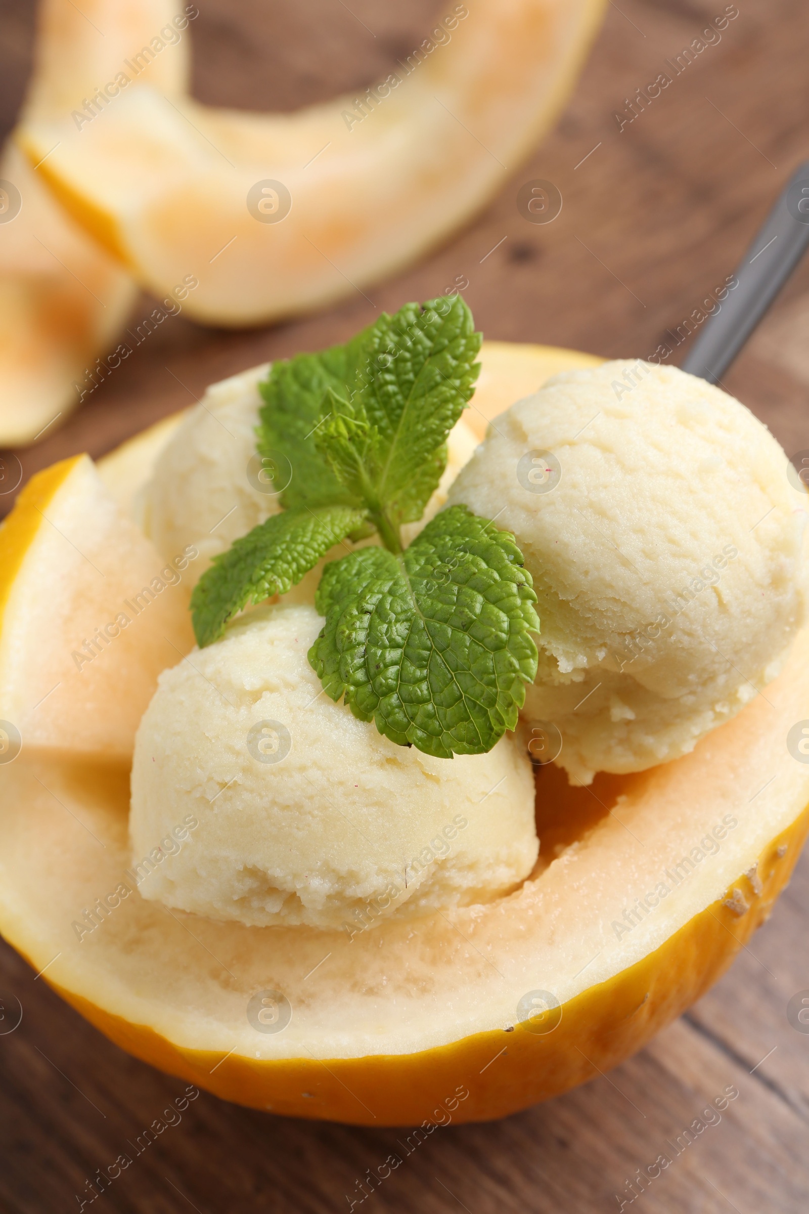 Photo of Scoops of tasty melon sorbet with mint in fresh fruit on wooden table, closeup