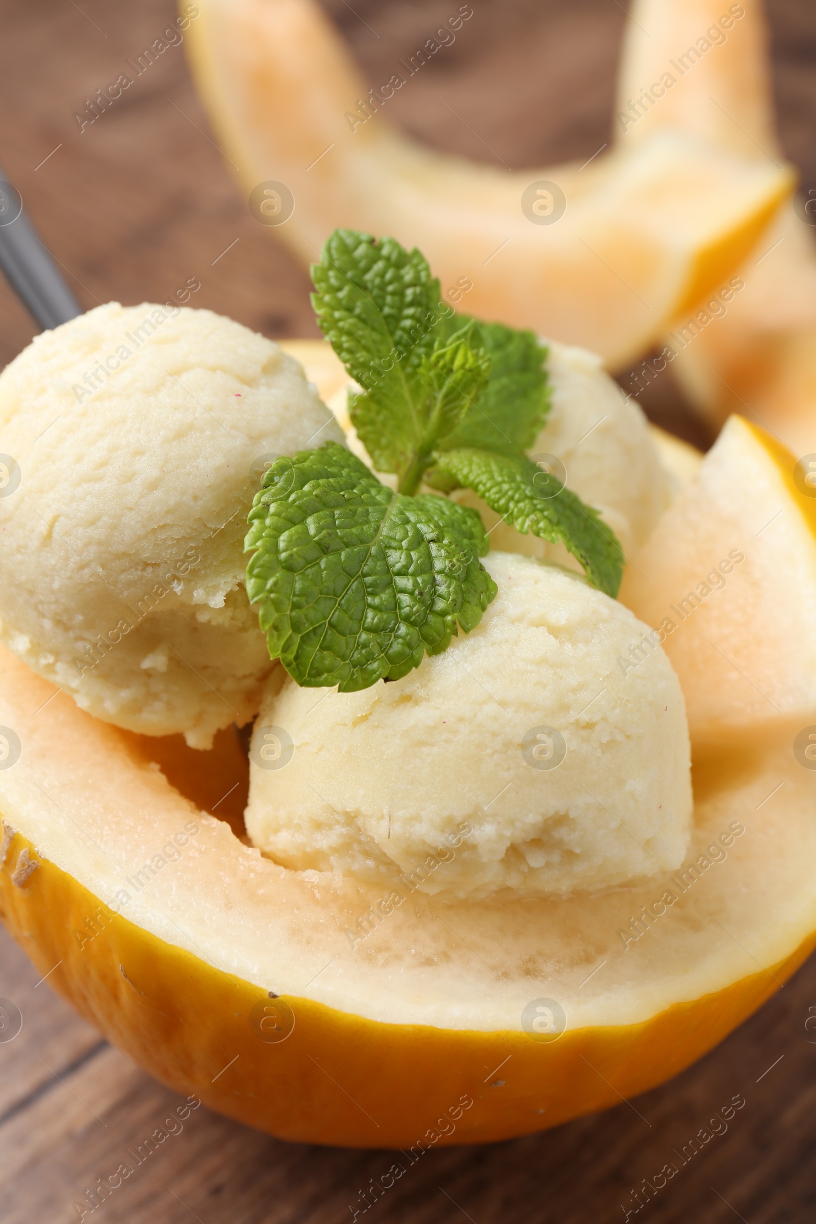 Photo of Scoops of tasty melon sorbet with mint in fresh fruit on wooden table, closeup