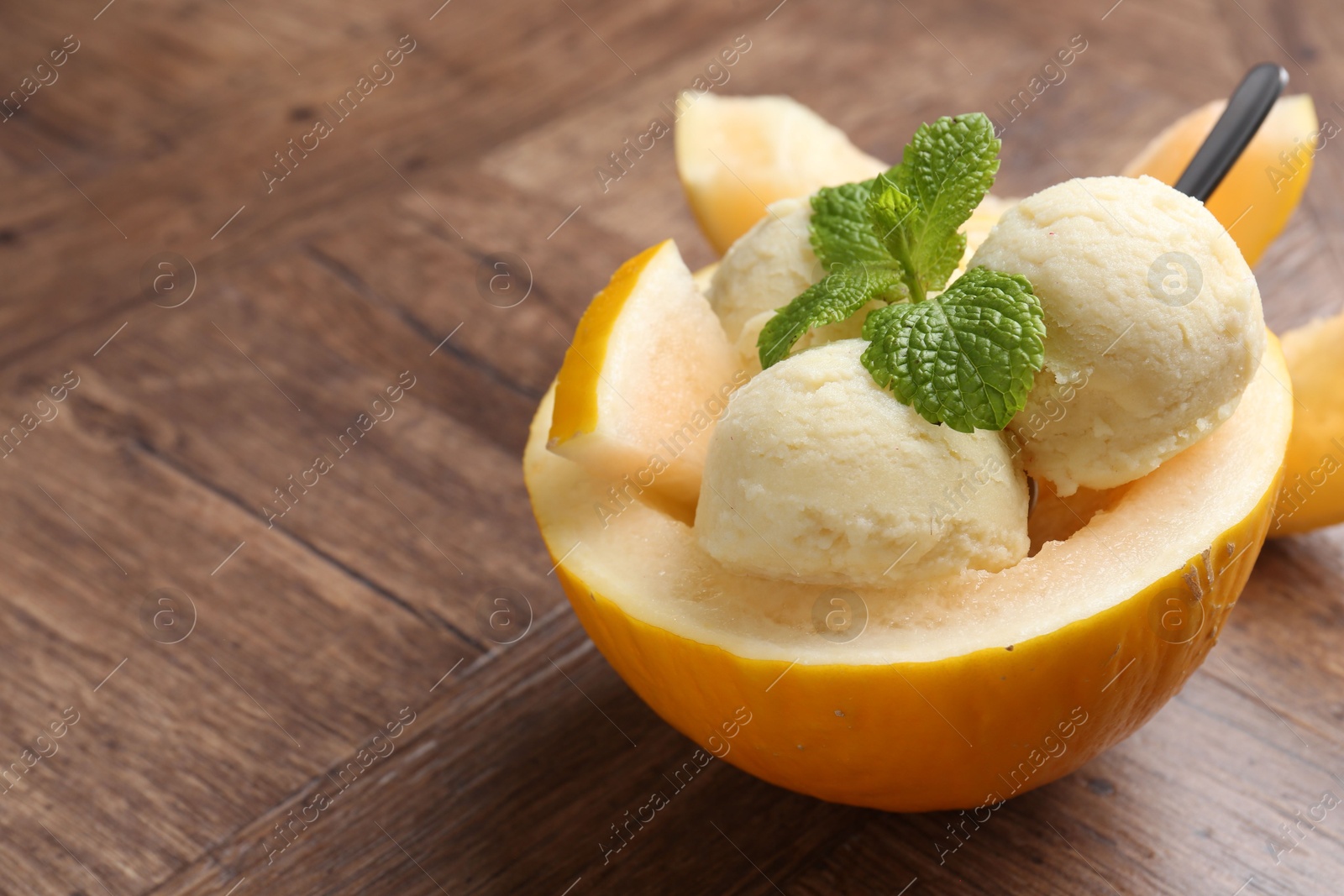 Photo of Scoops of tasty melon sorbet with mint in fresh fruit on wooden table, closeup. Space for text